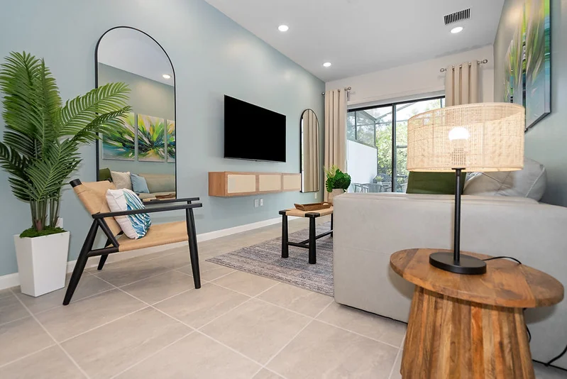 Compact light-oak desk against white wall, task chair, snake plant, arched-window view to Florida palm.