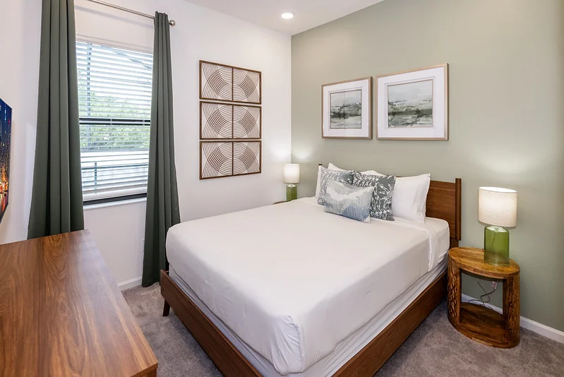 Resort-community condo guest room: queen bed, taupe accent pillows, single nightstand, low dresser.