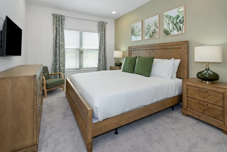 King bedroom with a wood panel headboard, white bedding and green accent pillows in the Paradiso Grande Ebb Tide Lane home