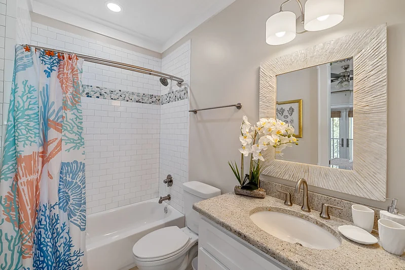 Condo bathroom vignette: white vanity, rectangular mirror, folded spa towels, single small coastal print.